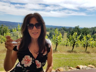 A smiling woman holding a glass of wine on the outdoor patio at Holly's Hill Winery in the El Dorado County foothills.