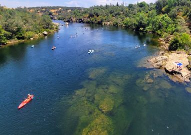 High angle view of people kayaking and stand-up paddleboarding on the clear blue water of Lake Natoma in Folsom California.